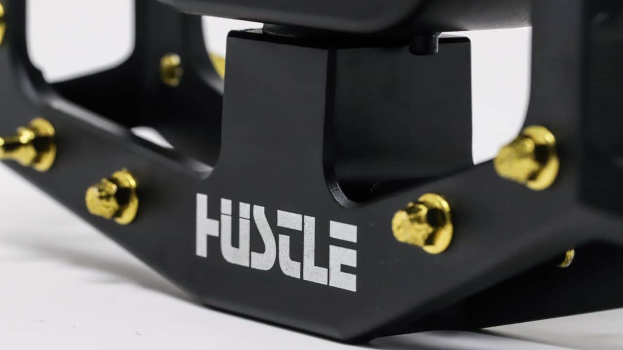 Detailed image of the engraved Hustle Bike Labs logo on the REMtech Blackjack Black pedal.