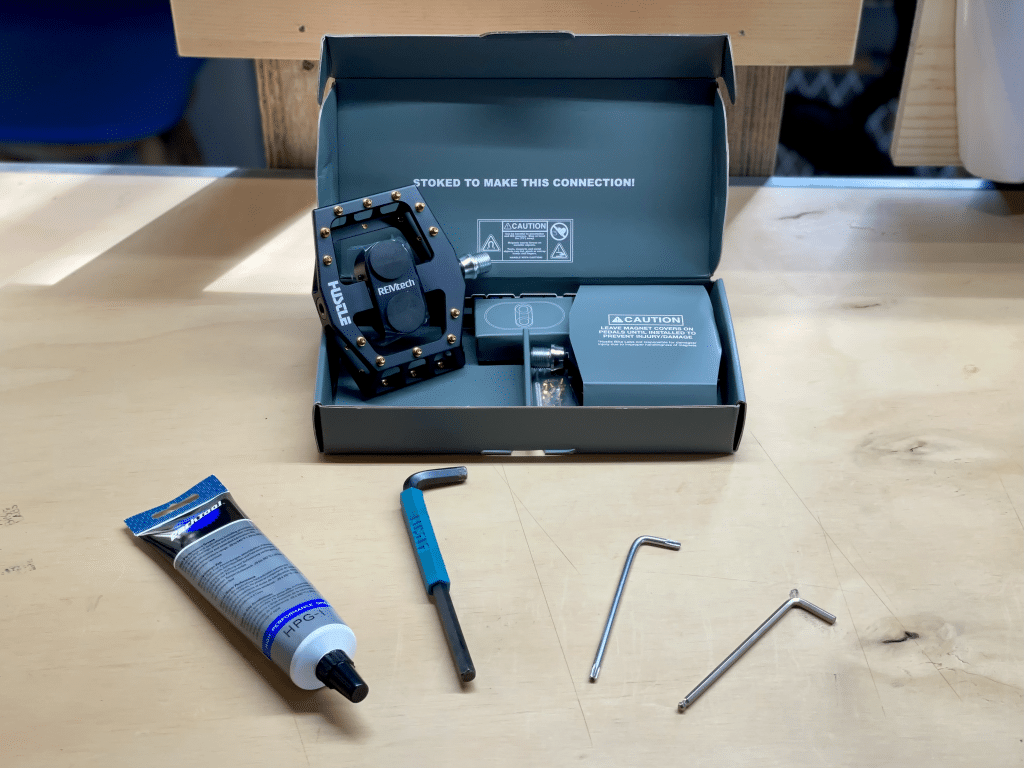 Image of REMtech pedals in box with the needed tools and accessories to install pedals. The need supplies are 8mm hex, grease, and 4mm hex or T-25 Torx. 