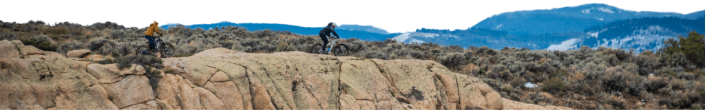 Scenic Colorado shot of to mountain bikers on a ridge line with snowy mountains in the background.