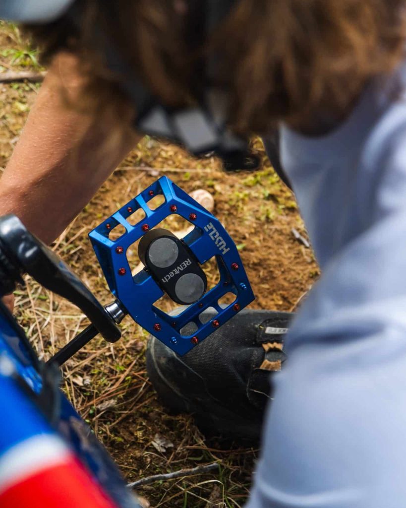 Close up peak through a rider's arms as he is installing his blue REMtech Magnetic Pedals on his MTB bike.